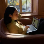 Woman using Silver Apple MacBook Air 13-inch M5 with 16GB RAM and 512GB SSD by window, ideal for professionals and creators.