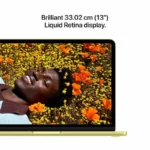 Apple MacBook Neo 13-inch Citrus laptop with 13" Liquid Retina display showing a person lying in a field of flowers.