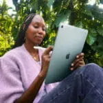 A woman holds an 11-inch Apple iPad Air M4 in Starlight finish while using an Apple Pencil in a lush outdoor setting.